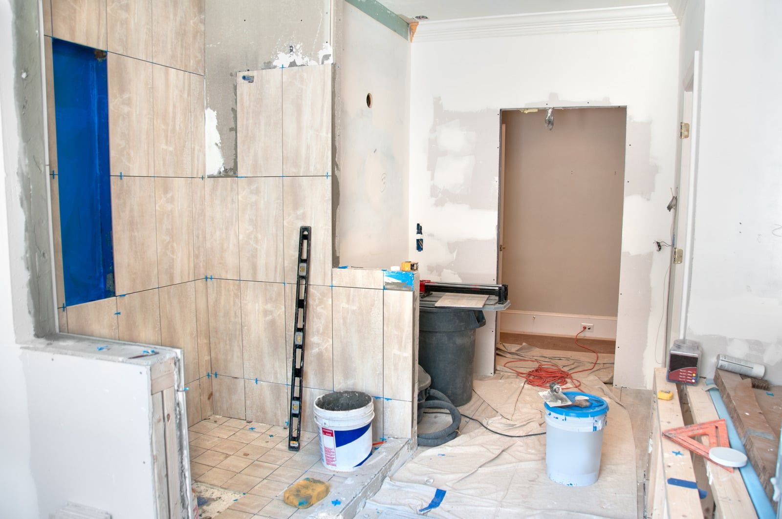 Badeværelse under renovering med halvt flisebelagte vægge, vaterpas og spande